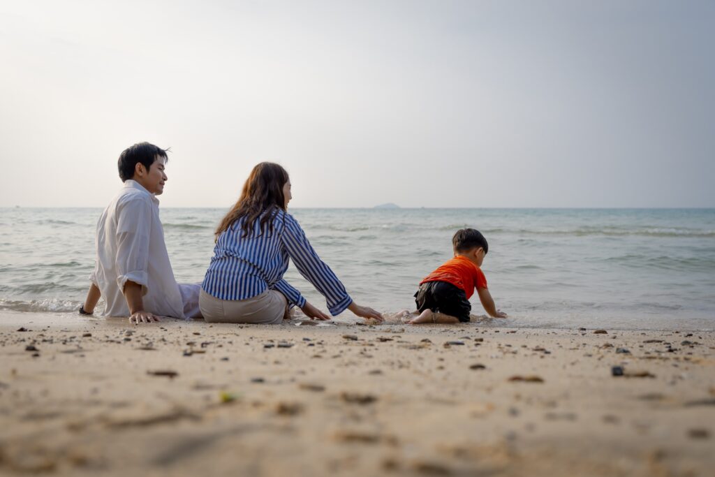 Happy family with a young son enjoying sunset on the beach, playing in the sand during summer vacation.