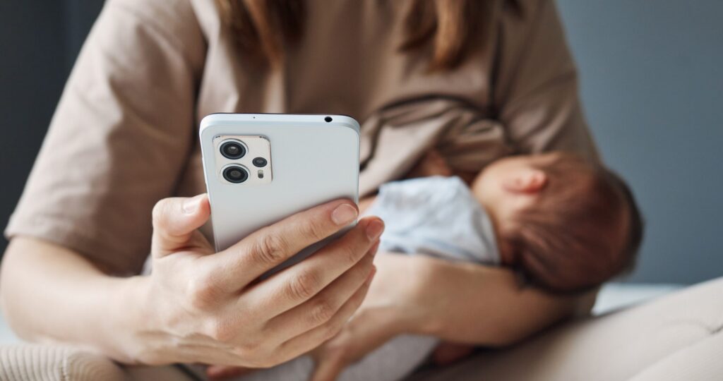 Unrecognizable unknown woman breastfeeding baby and using social media to stay in touch while maternity leave woman nursing child and holding smartphone